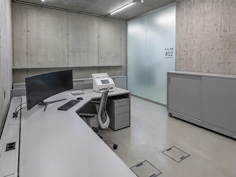 Aufgeräumter Büroarbeitsplatz mit Monitor und Drucker in einem Technikraum.