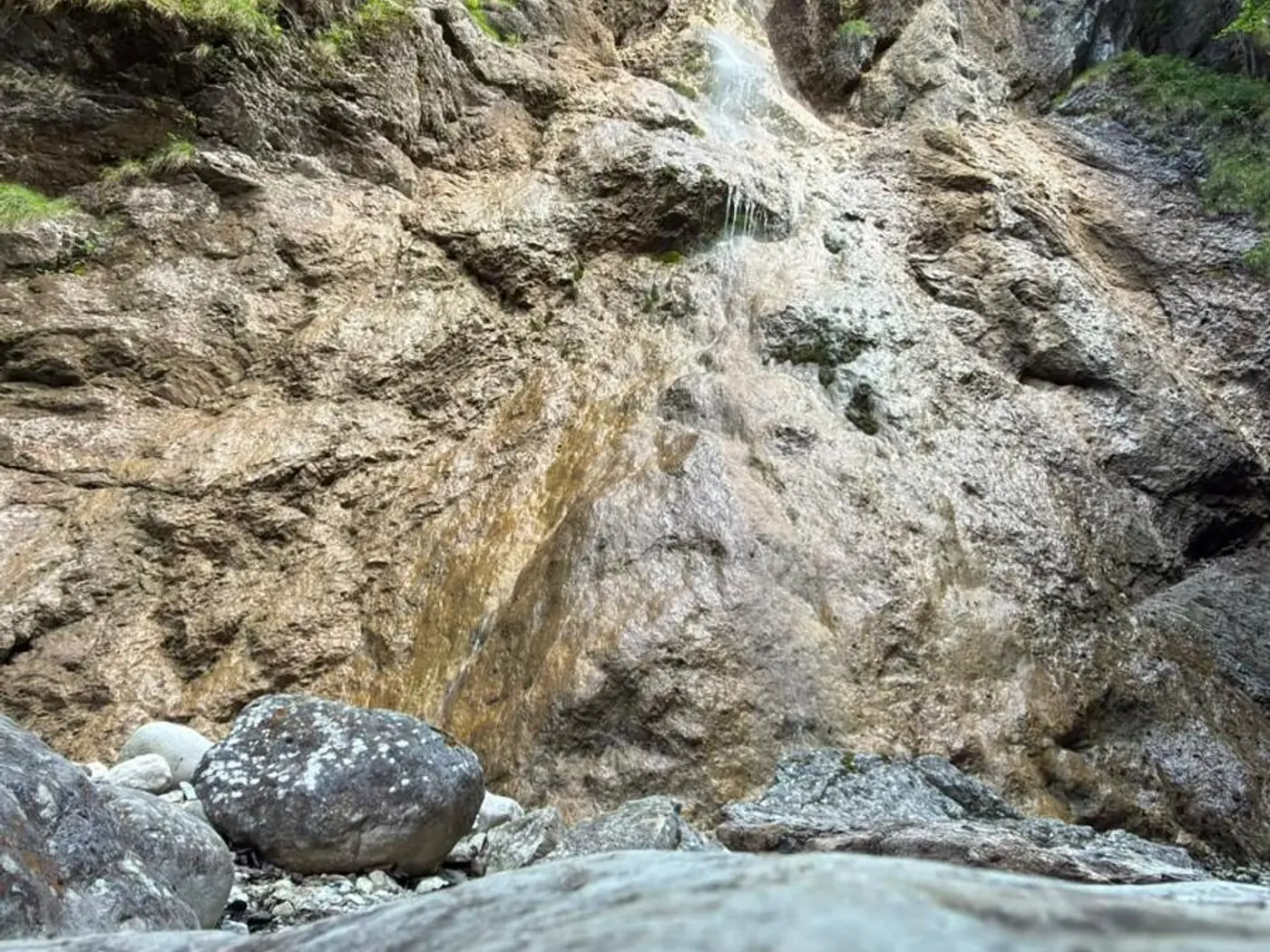 Wasser läuft über eine bewachsene Felswand und sammelt sich zwischen den Steinen darunter.